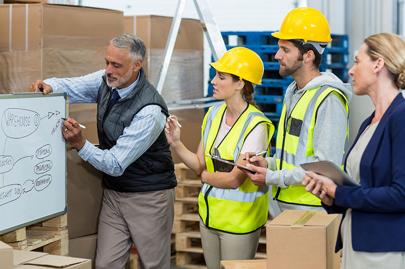 Manager and warehouse workers discussing over whiteboard